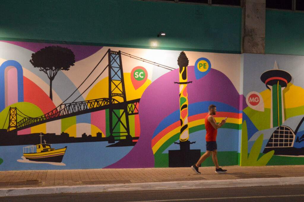 Mural colorido representando monumentos brasileiros com pedestres caminhando na Rua Augusta, em São Paulo.